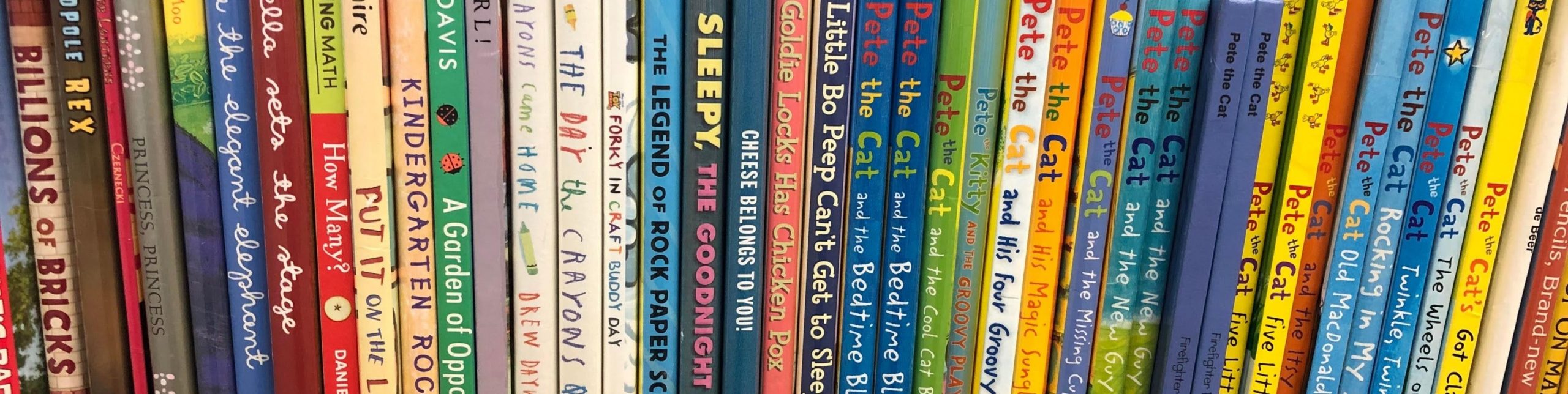 Colorful children’s books lined up on a shelf showing a variety of titles and authors